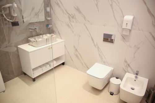 a white bathroom with a toilet and a sink at Sky Hotel Korce in Korçë