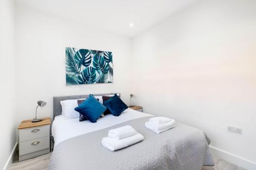 ein weißes Schlafzimmer mit einem Bett mit blauen Kissen in der Unterkunft Corby Town Centre Serviced Apartments in Corby