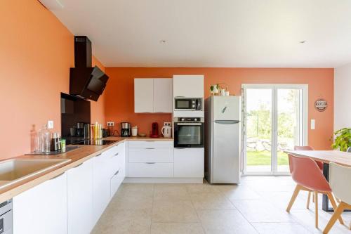 - une cuisine avec des placards blancs et un mur orange dans l'établissement LE CAMPALOU, à Saint-Barthélemy-le-Plain