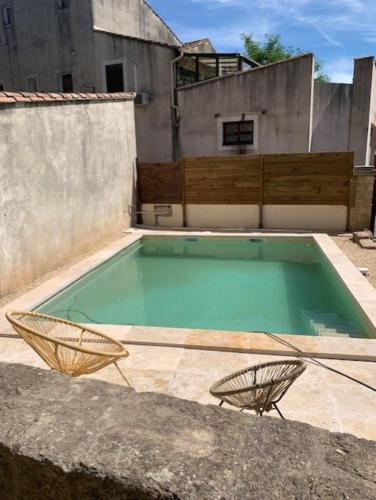 - une piscine avec 2 chaises en face d'un bâtiment dans l'établissement L'Ostal de Terralha avec piscine au centre du village, à Montfrin
