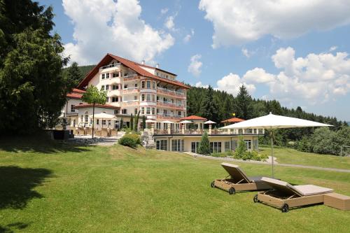 a large building with two lounge chairs and an umbrella at Ailwaldhof Parkhotel & Spa in Baiersbronn