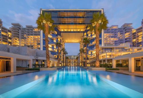 a large building with a swimming pool with palm trees at Maison Privee - Glamourous Apt with Sea Views at FIVE Palm in Dubai