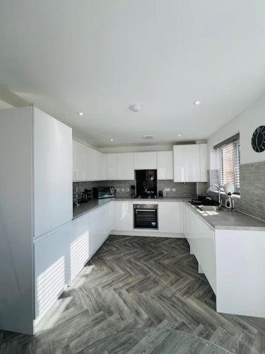 a kitchen with white cabinets and a wooden floor at Beautiful 3 Bed Detached House in Grimsby in Little Coates