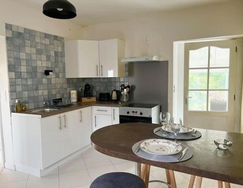 una cucina con armadi bianchi e un tavolo con bicchieri di Charmante maison Girondine a La Rivière