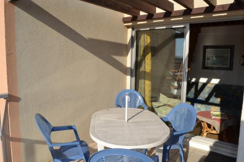 - une table blanche et des chaises bleues sur une terrasse couverte dans l'établissement 030 Jean Bart 54, au Cap d'Agde