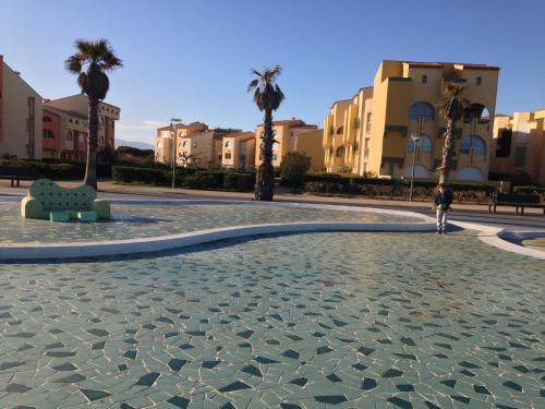 une personne debout dans une cour avec des palmiers dans l'établissement Les portes de la Plage, à Port-Leucate