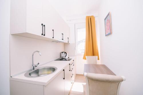 a white kitchen with a sink and a chair at Apartments Art in Ulcinj