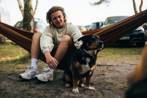 a man sitting in a hammock with a dog at Klimatyzowane Surf Domki - Maszoperia Sun4Hel - Letnia Baza SnowShow na Półwyspie Helskim in Jastarnia