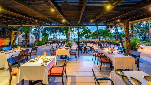 a restaurant with white tables and chairs and windows at Impiana Beachfront Resort Patong, Phuket in Patong Beach