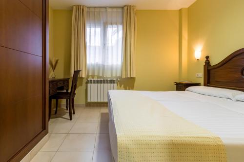 a bedroom with a bed and a desk and a window at Apartamentos Silken Playa de Toró in Llanes
