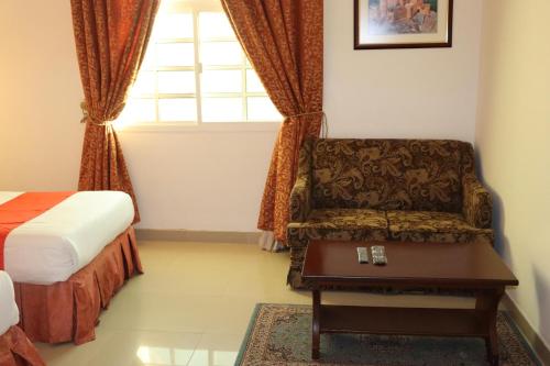 a bedroom with a bed and a chair and a window at Dahlia Sohar Hotel Apartments in Sohar