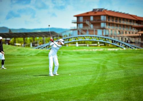 a woman swinging a golf club on a golf course at Villa Ambassadori Kachreti Golf Resort in Gurjaani