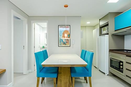 a kitchen with a white table and blue chairs at 7th Avenue - Apartamentos UROOMS in Curitiba