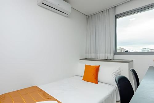 a bedroom with a bed and a table and a window at 7th Avenue - Apartamentos UROOMS in Curitiba