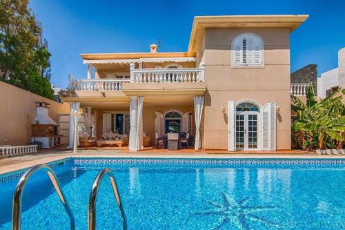 a villa with a swimming pool in front of a house at Bayside Concha House - Beachfront Oasis with Heated Pool in Playa Honda