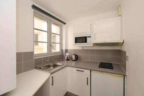 une cuisine blanche avec un évier et un micro-ondes dans l'établissement 202 - Studio calme et reposant a Paris 5 - FLAT-GUEST, à Paris