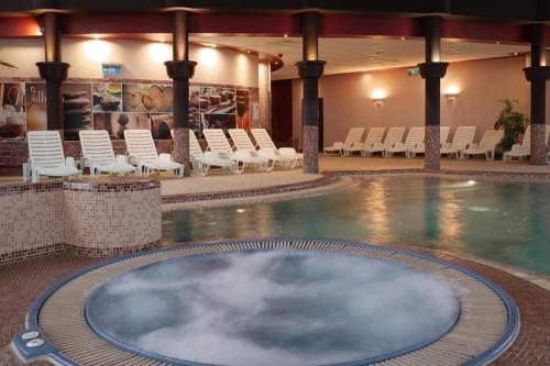 a large swimming pool with white chairs and a swimming poolasteryasteryasteryasteryastery at Wellness Park Apartman in Dunaszentmiklós