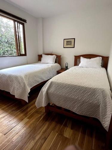 two beds in a room with wooden floors and a window at Hotel Campestre Ronda Ecuestre Rionegro in La Ceja