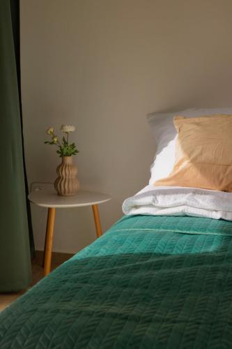 a bed with a green comforter and a table with a vase at Nyárfás Panoráma Vendégház in Dunavarsány