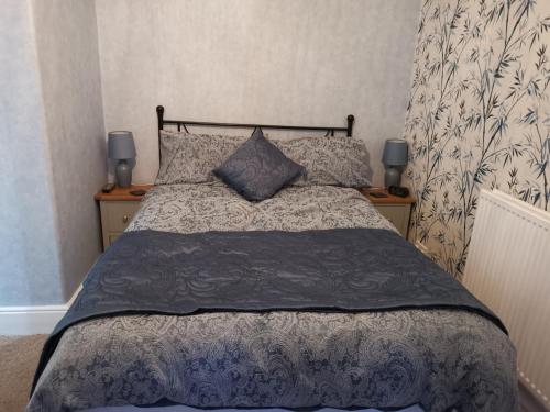 a bed with a blue comforter and two night stands at Brooklands Guest House in Bowness-on-Windermere