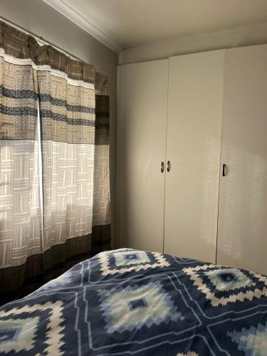 a bedroom with a bed and two windows with curtains at Nicole Guest Apartments in Germiston