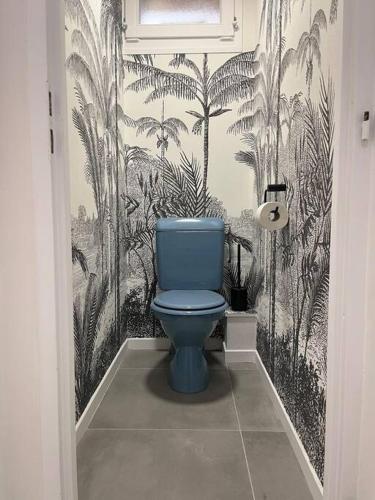 des toilettes bleues dans une salle de bain avec du papier peint à motifs de palmiers dans l'établissement La Pomme de Pin, à Le Biot