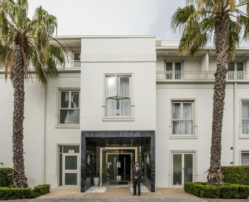 un homme debout devant un bâtiment blanc avec des palmiers dans l'établissement Queen Victoria Hotel by NEWMARK, au Cap