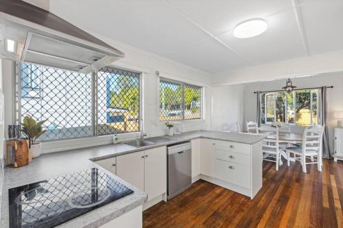 a kitchen with white cabinets and a dining room with a table at Warm and Cozy Cottage House in Gympie