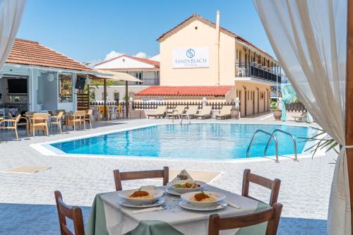 a table with food on it next to a swimming pool at Sandy Beach Complex - Poolside Studios & Seaside Apartments in Kavos