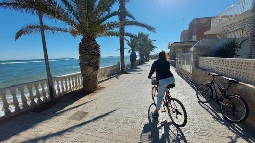 a woman riding a bike on a sidewalk near the beach at CHALET A 5 METROS DEL MAR.Wifi gratis in Murcia
