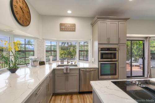 a kitchen with white cabinets and a large clock on the wall at Kaanapali Hini NEW POOL - FULLY REMODELED - Across the Street From Kaanapali Beach in Lahaina