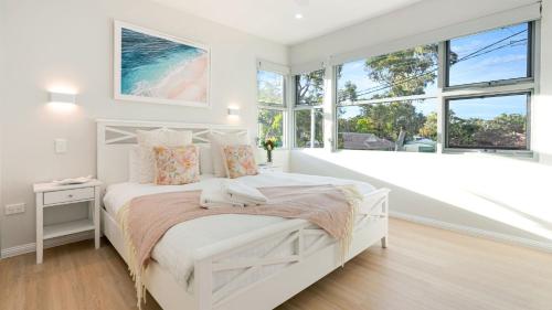 a white bedroom with a white bed and windows at Elliniko in Callala Beach