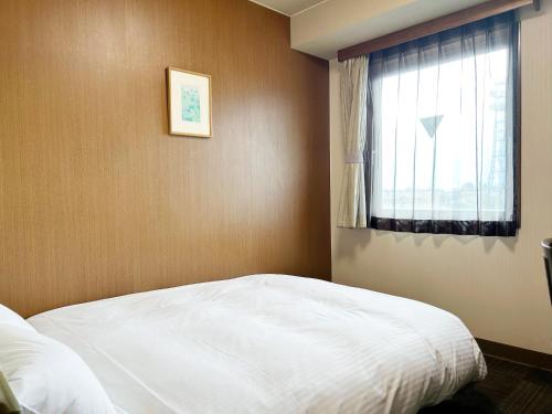 a bedroom with a white bed and a window at Hotel Route-Inn Court Kofu in Kofu