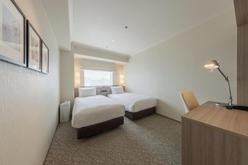 a hotel room with two beds and a desk at Hotel Associa Toyohashi in Toyohashi