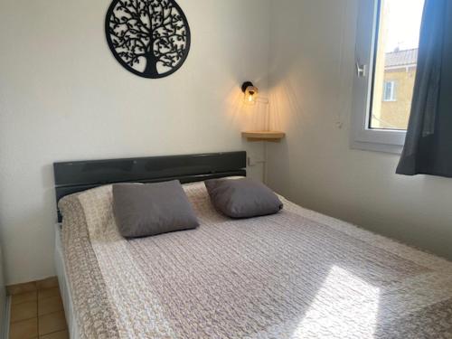 a bed with two pillows and a clock on the wall at Saint-Pierre-La-Mer : Appart T2 avec Piscine, Parking, Clim, Terrasse - 4 Pers. - FR-1-795-26 in Fleury