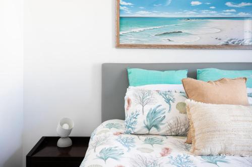 a bedroom with a bed with pillows and a painting at Mollymook Luxury Beachfront Apartment 10 in Mollymook