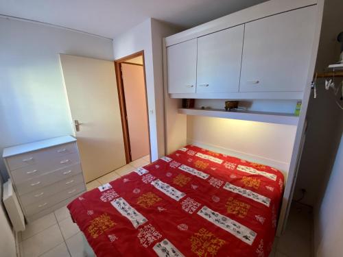 une petite chambre avec un lit rouge et des armoires blanches dans l'établissement T2 Confortable à Saint-Pierre-La-Mer - 4 Pers, Proche Plage, Tout Équipé, Balcon, Animations à Proximité - FR-1-795-47, à Fleury