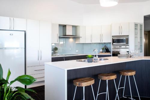 a kitchen with white cabinets and a counter with stools at Mollymook Luxury Beachfront Apartment 10 in Mollymook