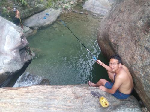 a man sitting on a rock holding a fishing pole at Tathagata Farm in Darjeeling