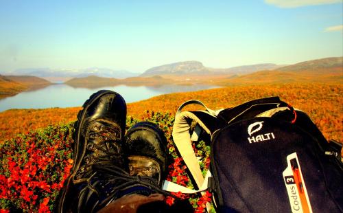a persons shoes and a backpack with a view of a lake at Saivaara Cottages in Kilpisjärvi