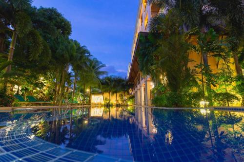 a swimming pool in front of a building with palm trees at Thanthip Beach Resort Patong in Patong Beach