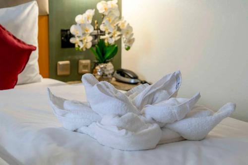 a pile of towels on a bed with a vase of flowers at PLAZA INN Blankenburg Ditzingen, Sure Hotel Collection in Ditzingen
