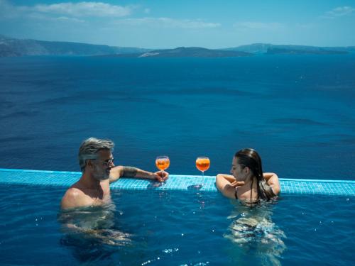 a man and a woman in the water with wine glasses at Santorini Secret Suites & Spa, Small Luxury Hotels of the World in Oia