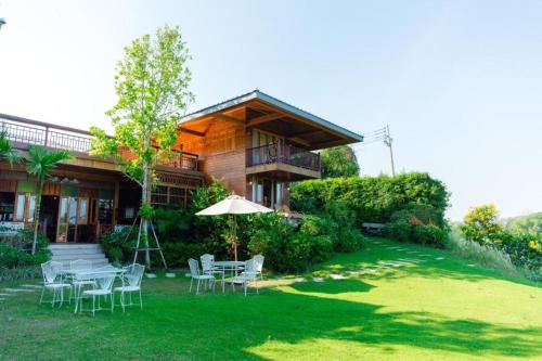 a house with chairs and an umbrella in the yard at Burann Bangtanode in Ratchaburi