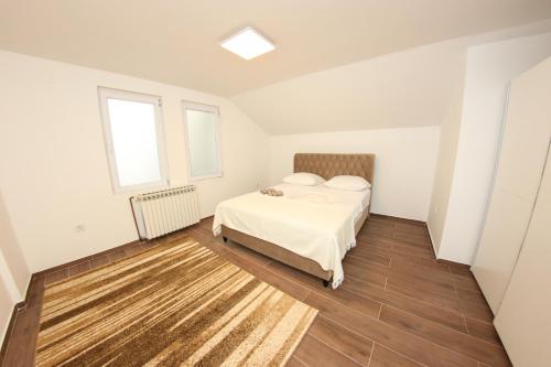 a white bedroom with a bed and two windows at Apartments Villa Begić in Sarajevo