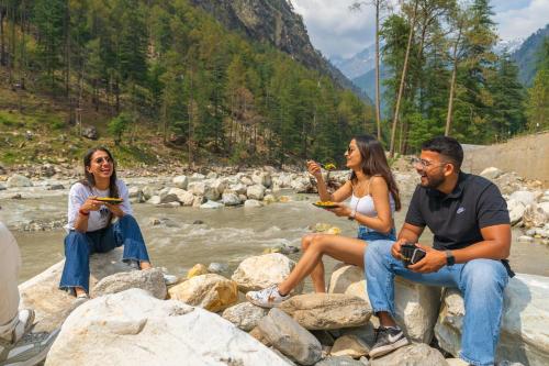 a group of three people sitting on rocks by a river at The Social Stays Kasol formerly ArtBuzz in Kasol