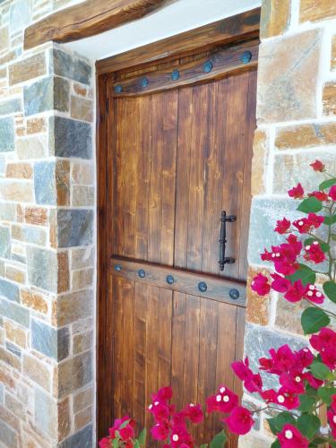 a wooden door in a stone wall with red flowers at The Cocoon and olives Hut in Koropi