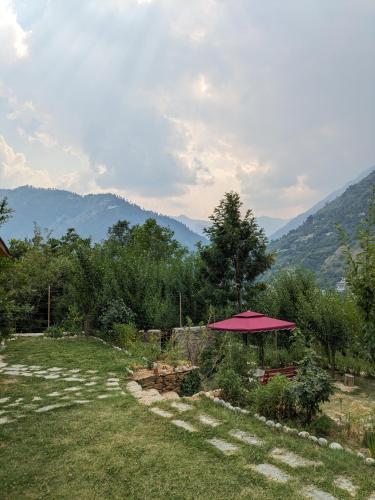 a picnic table with a red umbrella in a field at Aashirwad Homestay Kullu in Kulu