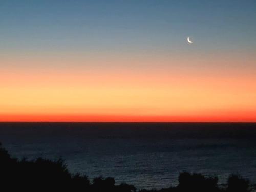 a sunset with the moon in the sky over the ocean at Hallett Cove Hideaway By Host Solutions in Halletts Cove