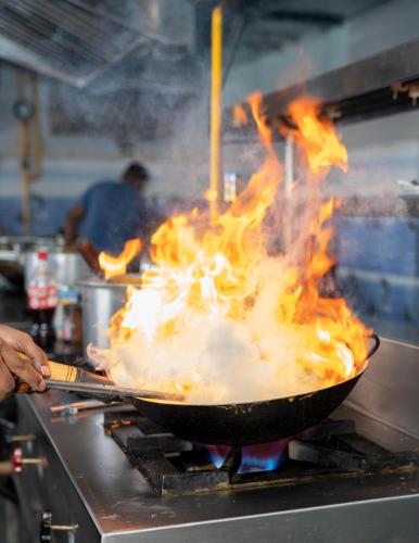 a person cooking food in a wok with flames at Hotel W Grand - A Boutique Hotel in Haridwār
